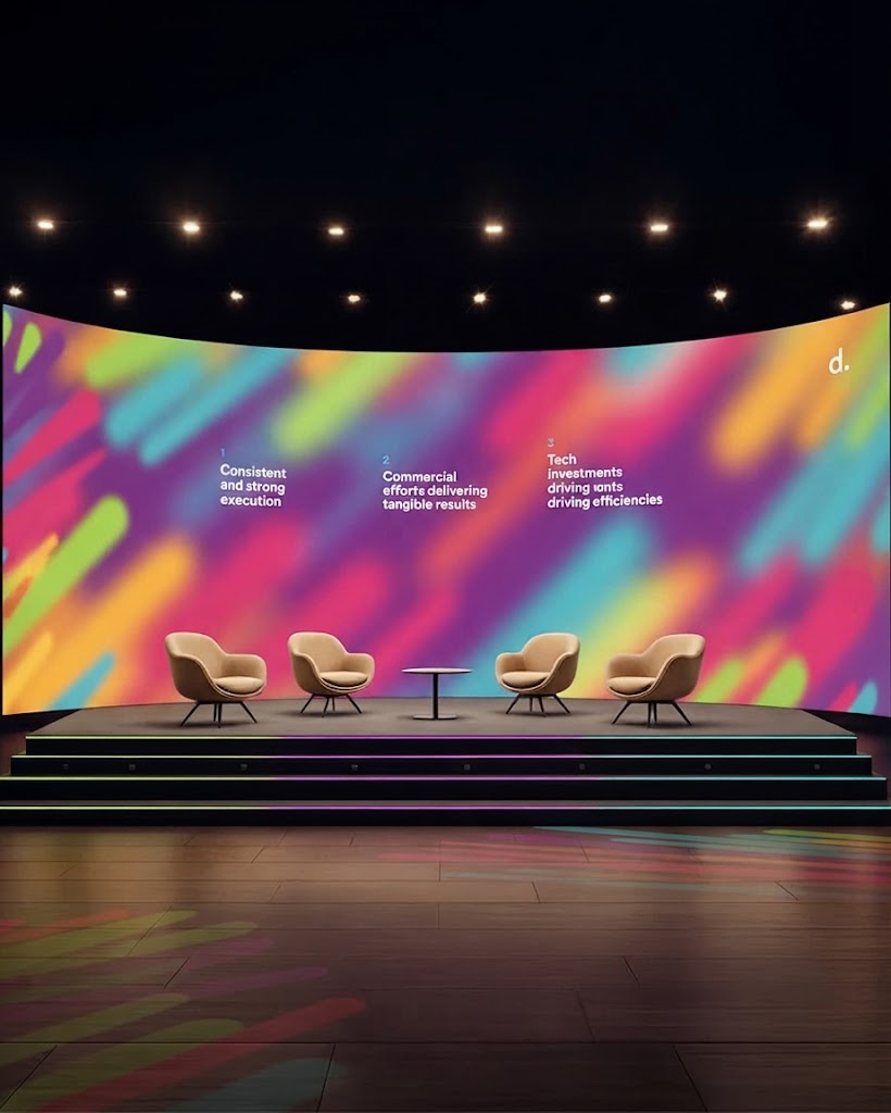 Dark corporate presentation stage with curved blue LED backdrop and lounge chairs