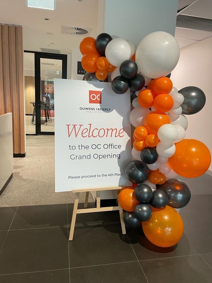 Orange, black, and white balloon garland beside a grand opening welcome sign