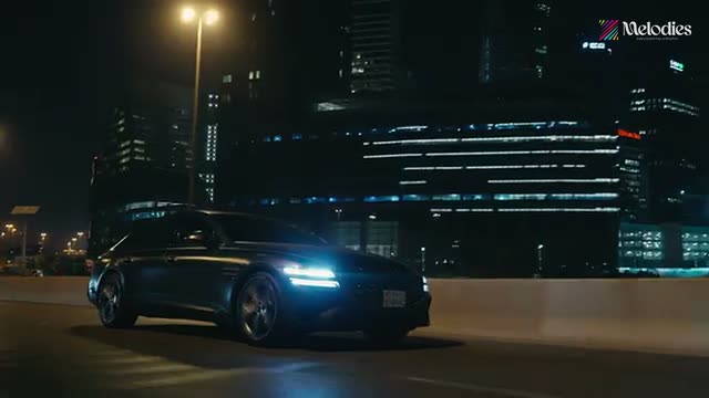 Luxury sedan driving at night against a lit city skyline